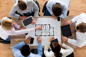 business, people, technology and team work concept - close up of architects with blueprint, smartphones and tablet pc computers sitting at table in office